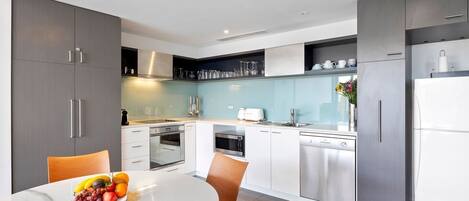 A modern kitchen with grey cabinets, white countertops, and stainless steel appliances.