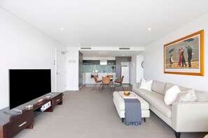 Een moderne woonkamer met een flatscreen televisie, een bank en een eethoek met stoelen en een tafel.