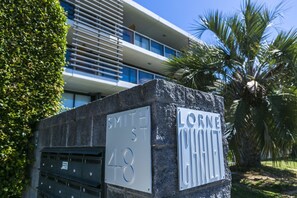 Een gebouw met een moderne architectuur, herkenbaar aan het platte dak en de grote ramen. Twee straatnaambordjes geven 'Smith St' en 'Lorne Ct.' aan.