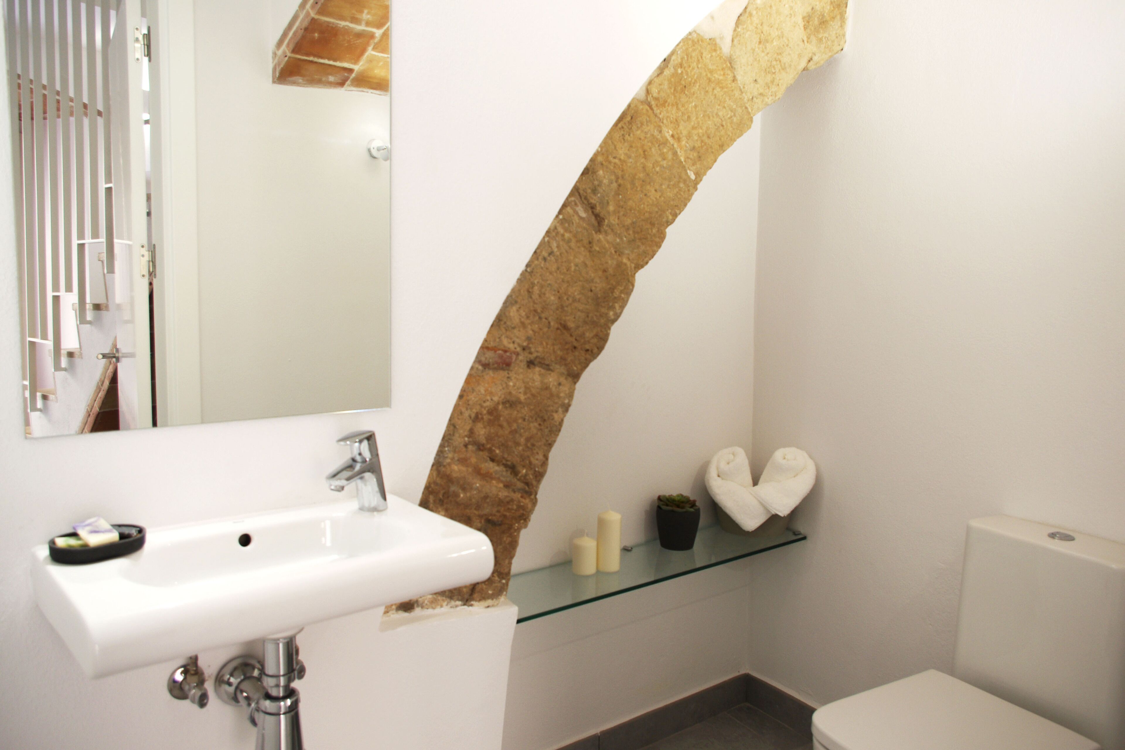 Un baño con un lavabo blanco, un estante de vidrio con artículos de aseo, un espejo y un inodoro.