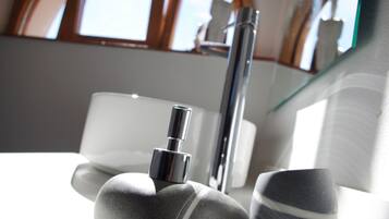 A bathroom with a modern design, featuring a chrome faucet, a white sink, and a glass shower enclosure.