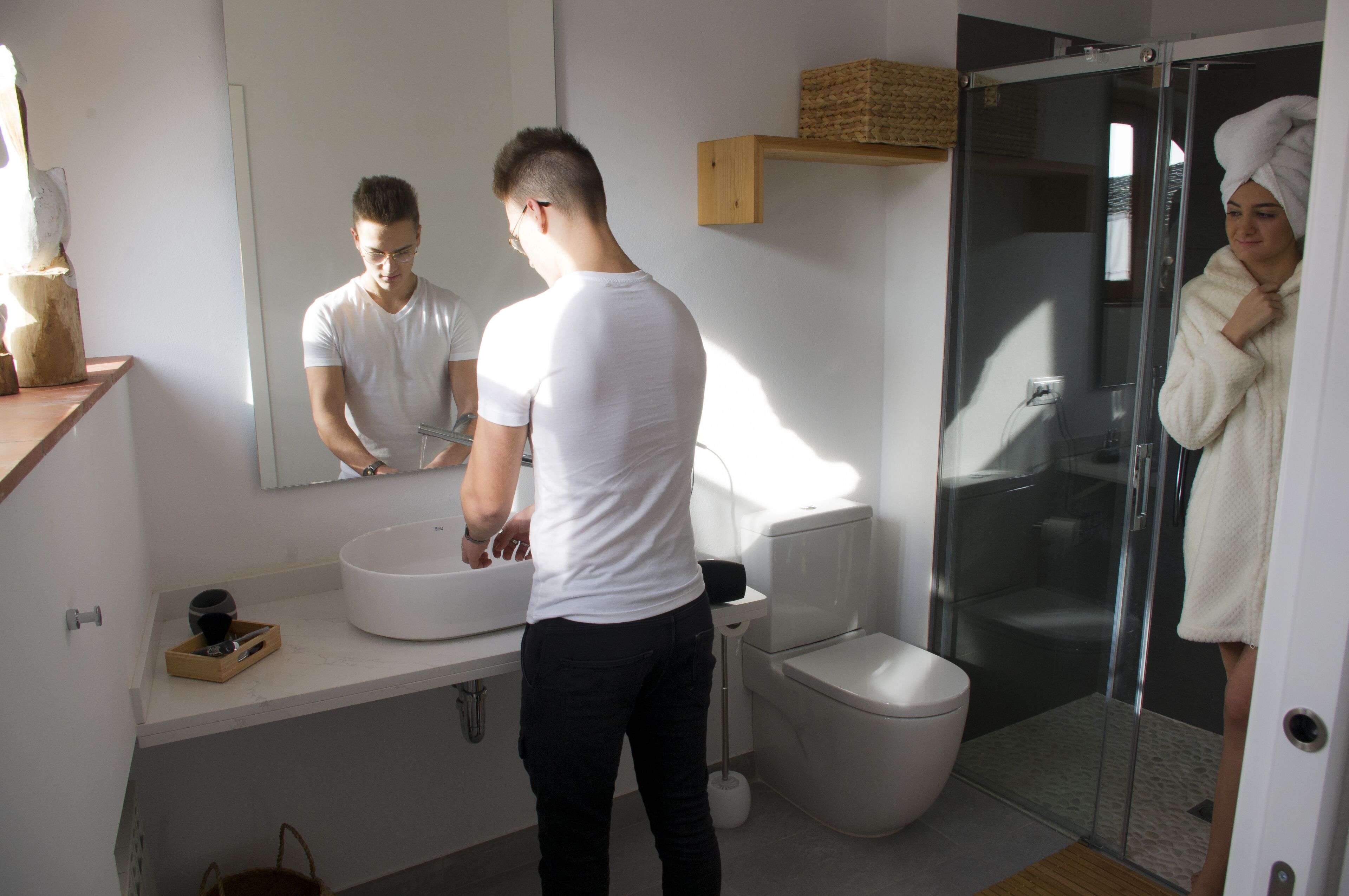 Un baño moderno con un espejo grande, lavamanos blanco y cabina de ducha de vidrio.