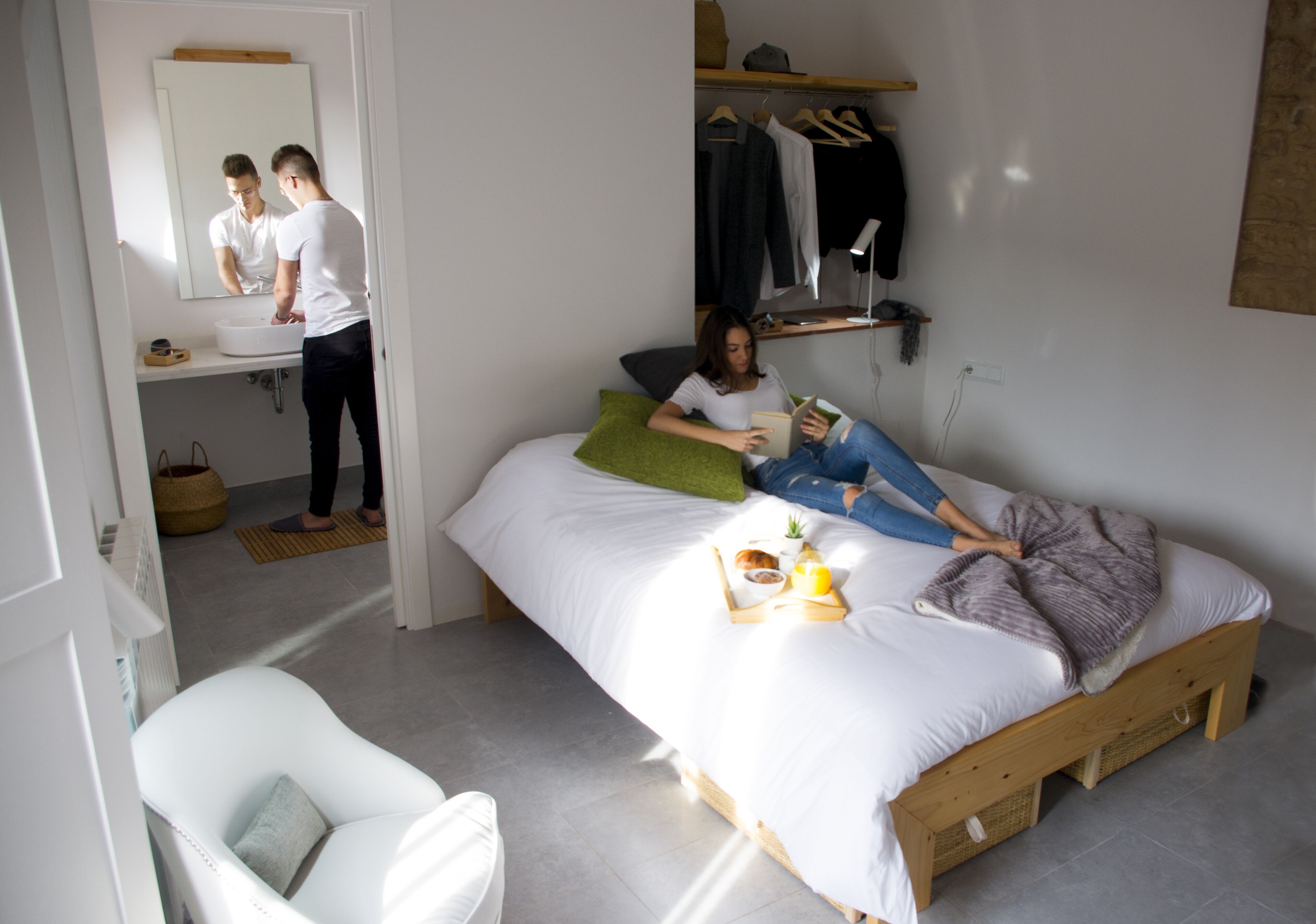 Une chambre à coucher avec un lit, une table de chevet sur laquelle se trouve un plateau avec des articles pour le petit-déjeuner, un miroir, une lampe suspendue et un portant à vêtements.