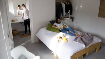 Une chambre à coucher avec un lit, une table de chevet sur laquelle se trouve un plateau avec des articles pour le petit-déjeuner, un miroir, une lampe suspendue et un portant à vêtements.