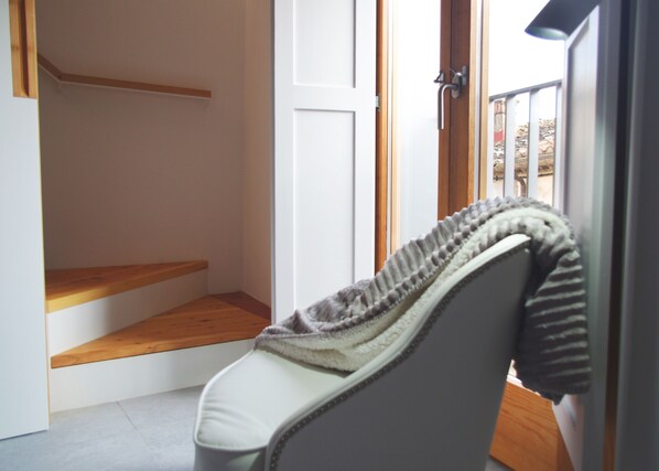 A room with a white chair, a wooden bench, a white door, and a window with a view of the outside.