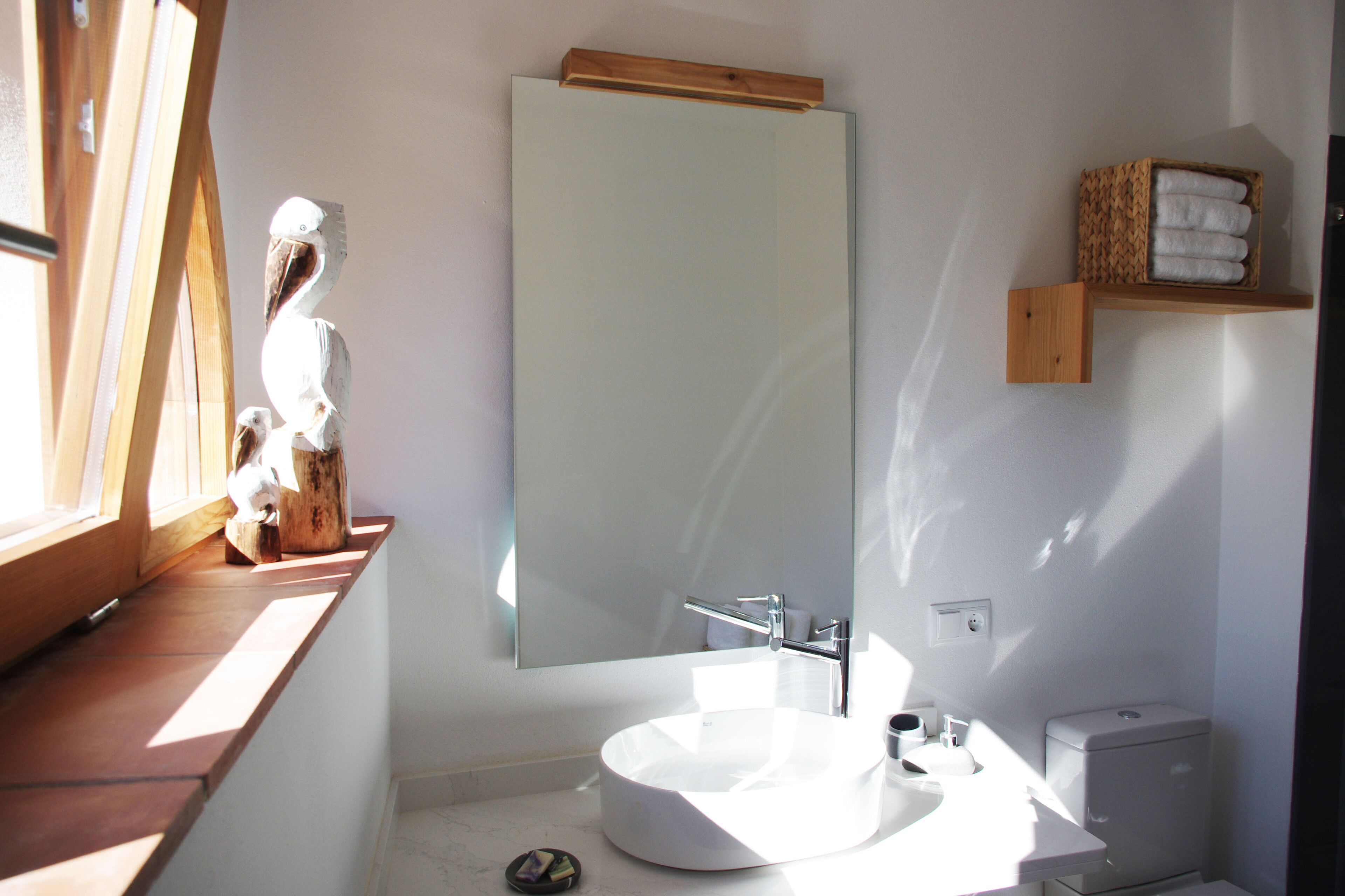 Un bagno con un lavandino bianco rotondo, uno specchio grande e uno scaffale di legno con asciugamani.