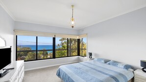 Un dormitorio con una cama grande, un escritorio y una silla, una ventana con vista al mar y una lámpara en el techo.