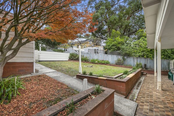 A residential backyard with a lawn, garden beds, and a barbecue area.