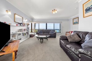 A living room with a leather sofa, a glass coffee table, a bookshelf, and a television. - Retro Retreat (Lorne)