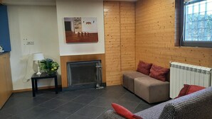 Un salón con chimenea, un sofá, una mesita con una lámpara y un ventanal con vistas a la vegetación.