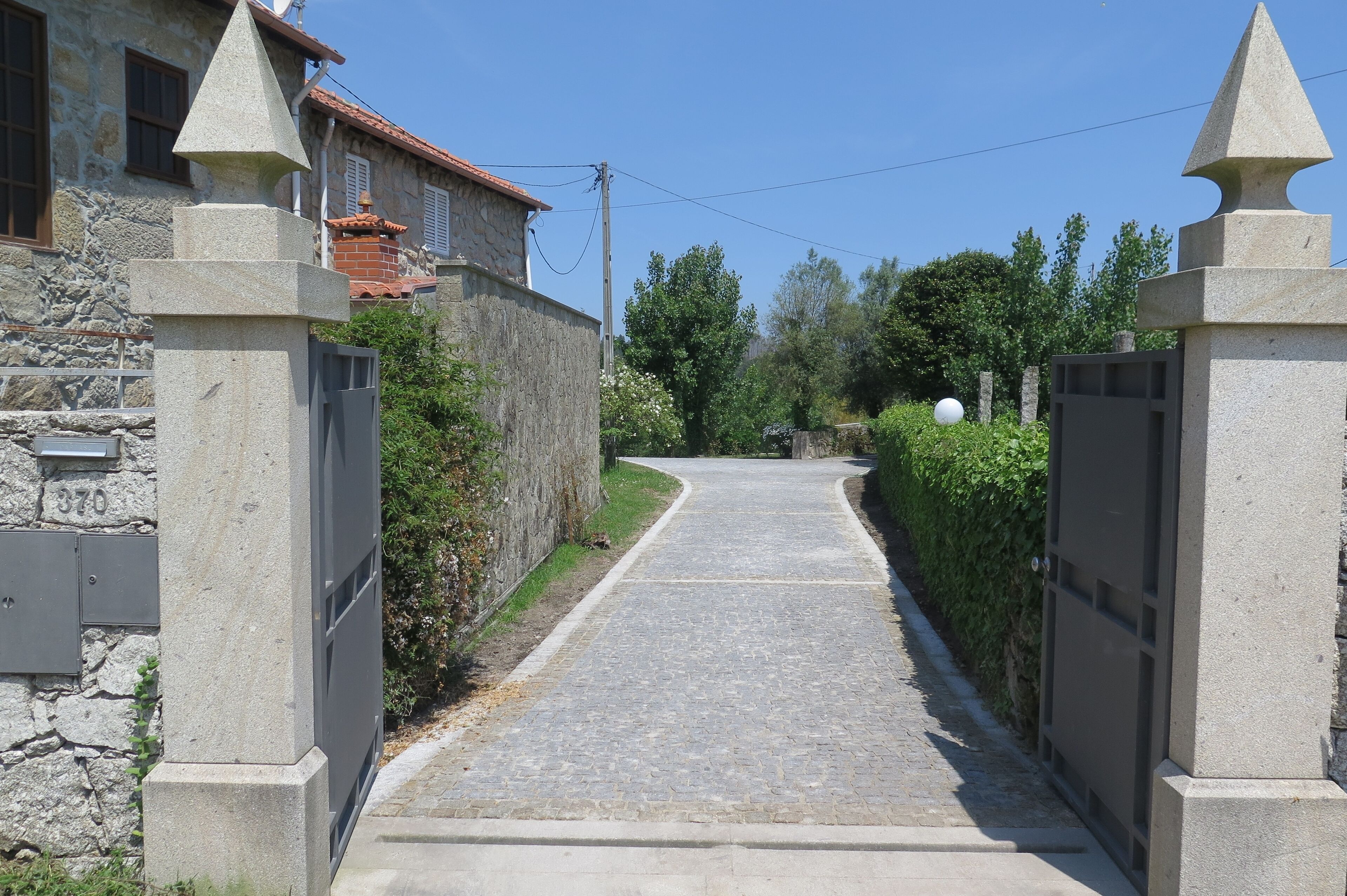 Un vialetto lastricato delimitato da mura in pietra e un cancello in metallo, che conduce a un edificio con facciata in pietra e tetto in tegole rosse.