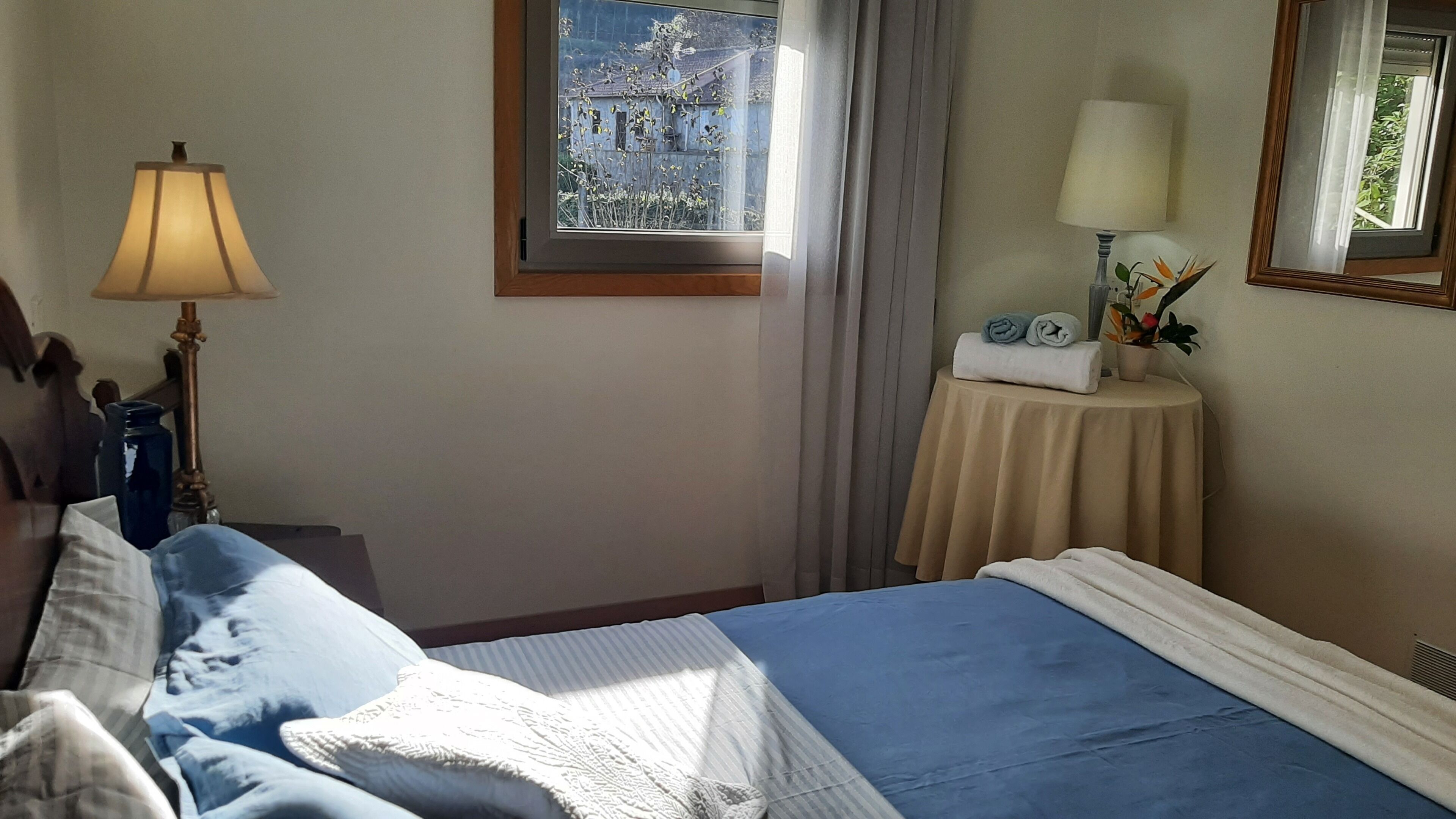 Ein Schlafzimmer mit einem Bett, einem Nachttisch, einer Lampe, einem Fenster mit Blick und einem Spiegel.