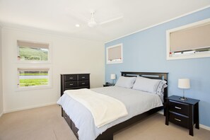 A bedroom with a bed, two nightstands, a ceiling fan, and two windows with blinds.