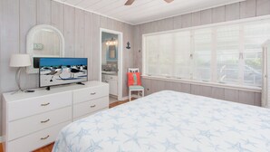 Un dormitorio con cama, cómoda, televisor, ventilador de techo y ventana con persianas.