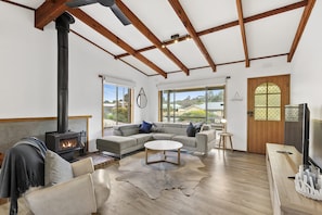 A spacious living room with a fireplace, large windows, and a cozy seating area. - The Beach Hut (Anglesea)