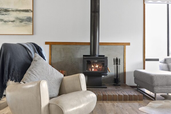 A modern living room with a wood-burning stove, leather armchairs, and a minimalist design. - The Beach Hut (Anglesea)