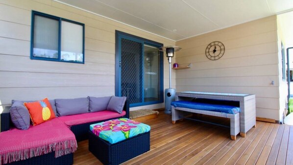 A covered outdoor seating area with a sofa, ottoman, and bench.