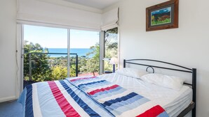 A bedroom with a bed, a window with a view of the sea, and a framed picture on the wall. - Seamist - Elevated With Amazing Outlook (Lorne)