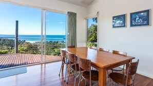 A dining area with a wooden table and chairs, large windows with a view of the ocean, and two framed pictures on the wall. - Seamist - Elevated With Amazing Outlook (Lorne)