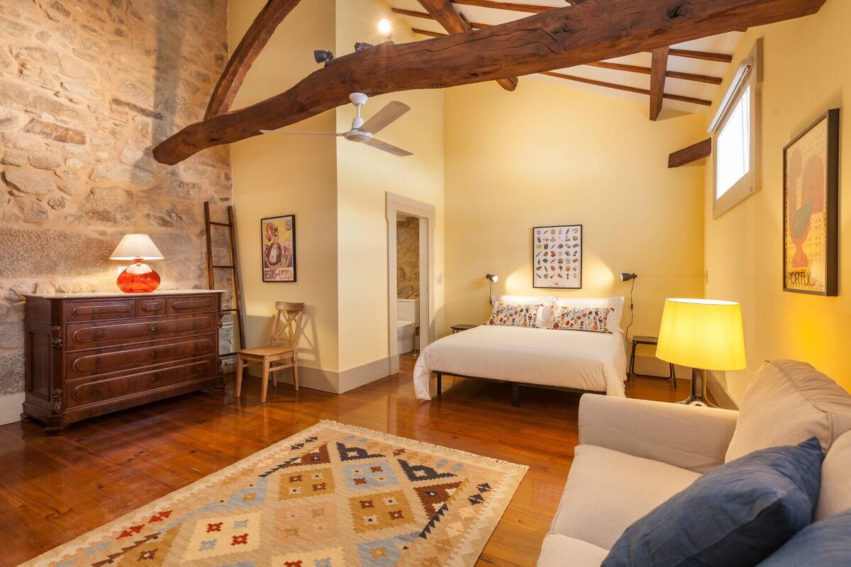 A cozy bedroom with a wooden dresser, a bed with patterned pillows, a chair, and a rug.