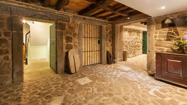 A stone-walled room with a wooden ceiling, a stone floor, and a green door leading to another room. - Casa Grande - Minho's Guest (Braga)
