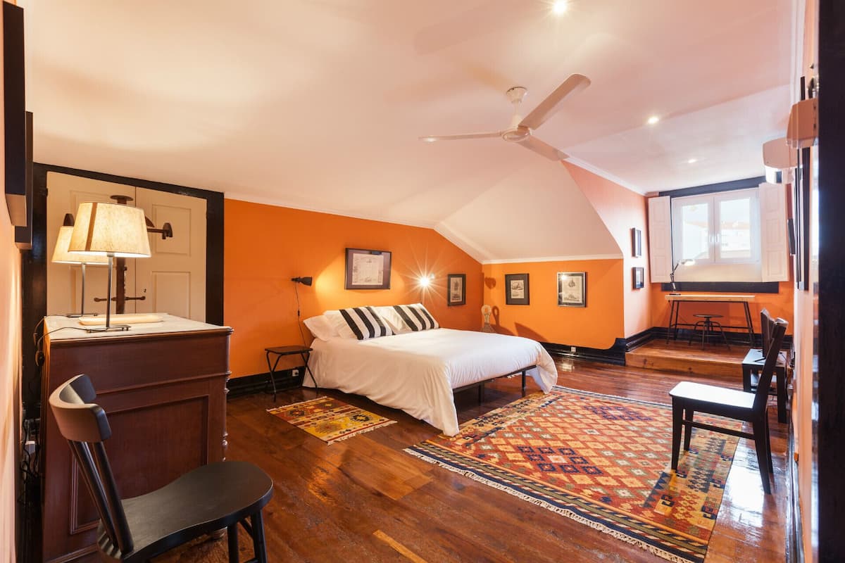 A bedroom with a bed, a desk, a chair, a ceiling fan, and a window.