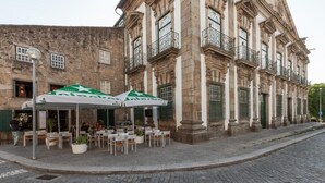 An outdoor café with tables and chairs, set against a historic building with stone walls and balconies. - Casa Grande - Minho's Guest (Braga)