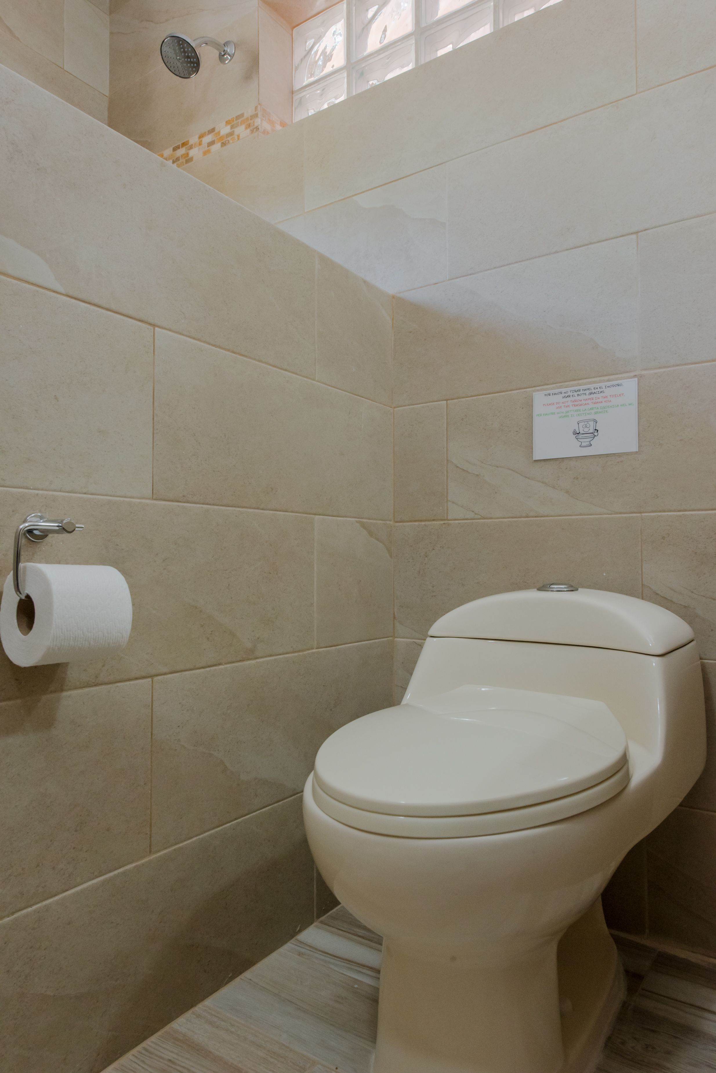 A bathroom with beige tiles, a toilet, a showerhead, and a toilet paper holder.