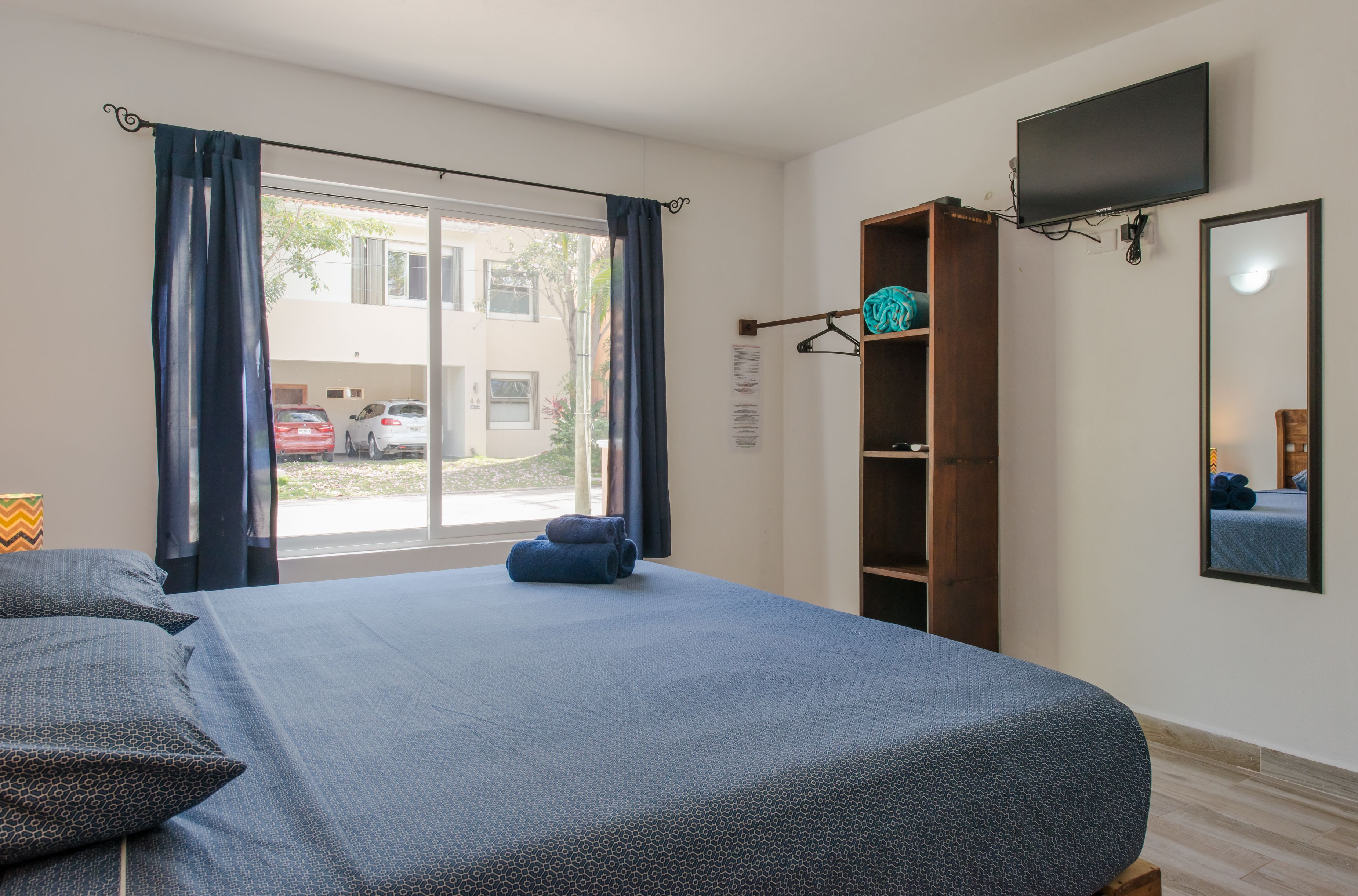 Une chambre à coucher avec un lit, une armoire, une télévision et une fenêtre avec des rideaux.