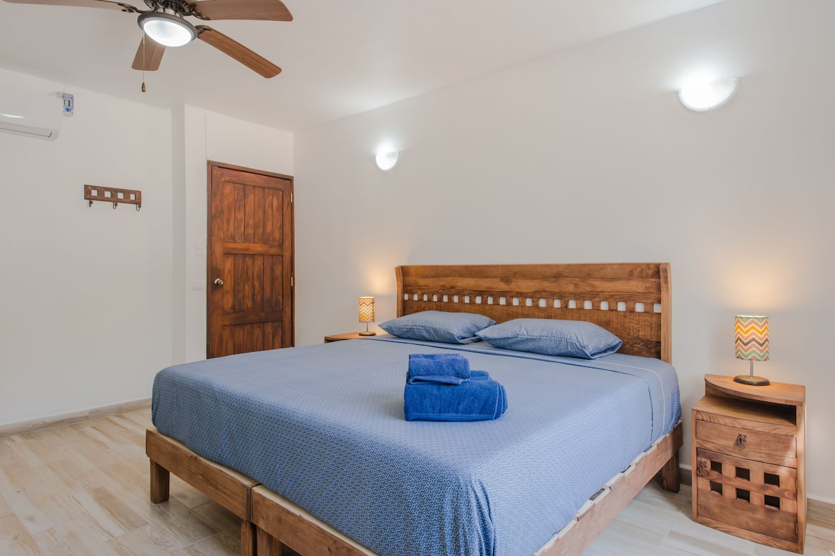 Un dormitorio con cama de madera, dos mesitas de noche, ventilador de techo y armario de madera.