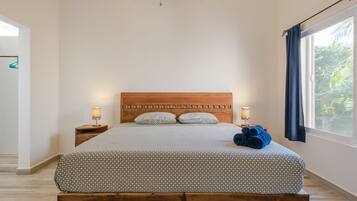 A bedroom with a wooden bed, two bedside tables, a window with curtains, and a view of greenery outside.
