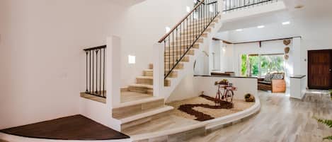 Un interior espacioso con una escalera curva, un pequeño jardín y un área de descanso con vistas al exterior.