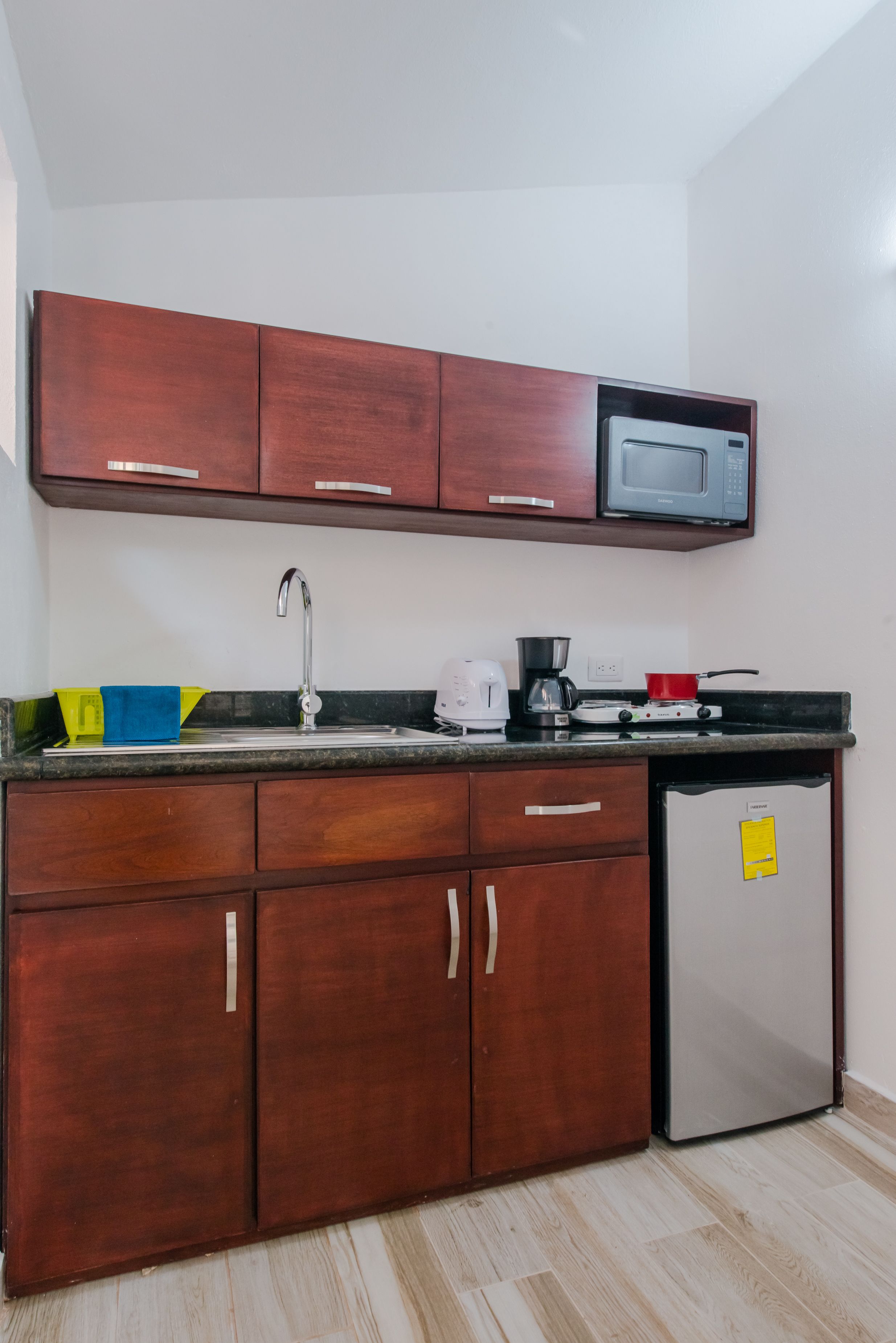 A compact kitchen with wooden cabinets, a stainless steel refrigerator, a microwave, a sink, and a gas stove.