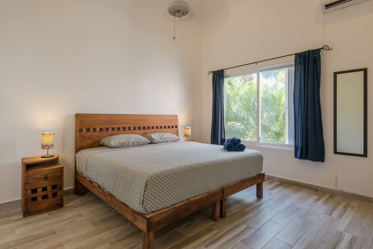 Un dormitorio con una cama de madera, una mesita de noche con lámpara y una ventana con cortinas.
