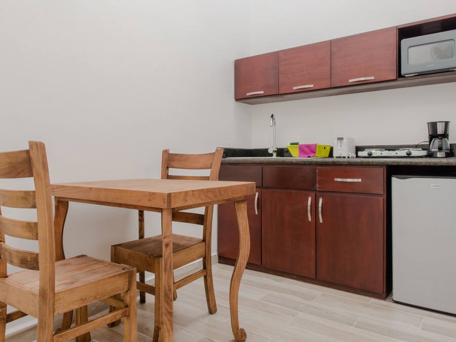 A compact kitchen with wooden chairs, a small dining table, and a microwave above the counter.