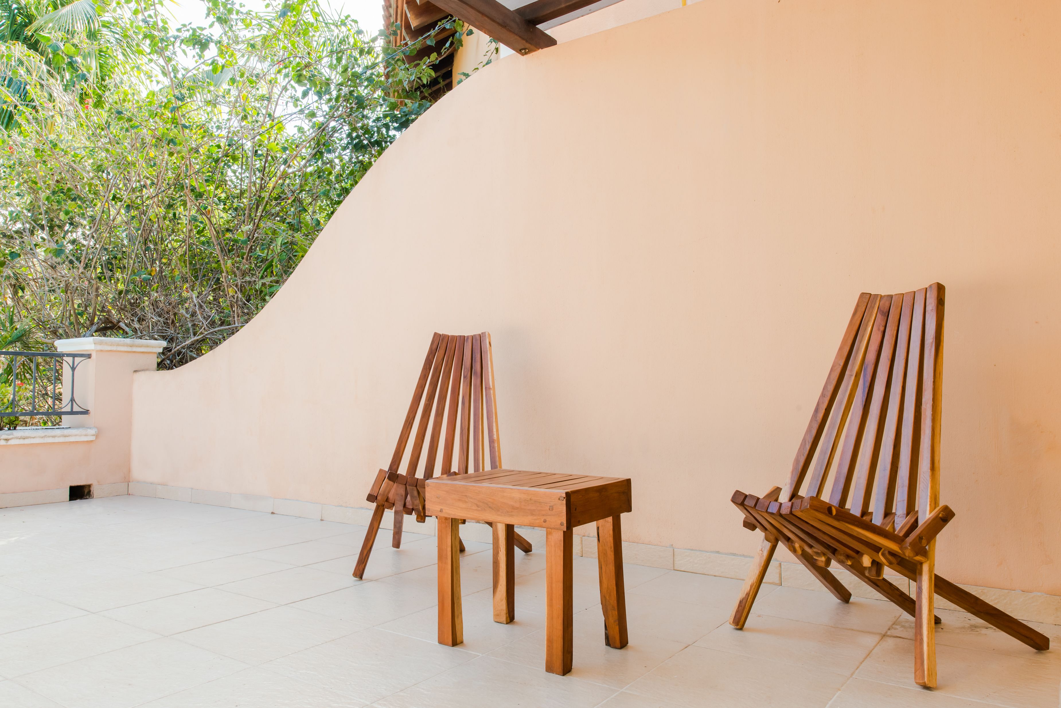 A wooden chair and table set against a wall with a tiled floor and a view of greenery.