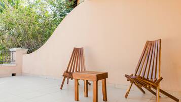 A wooden chair and table set against a wall with a tiled floor and a view of greenery.