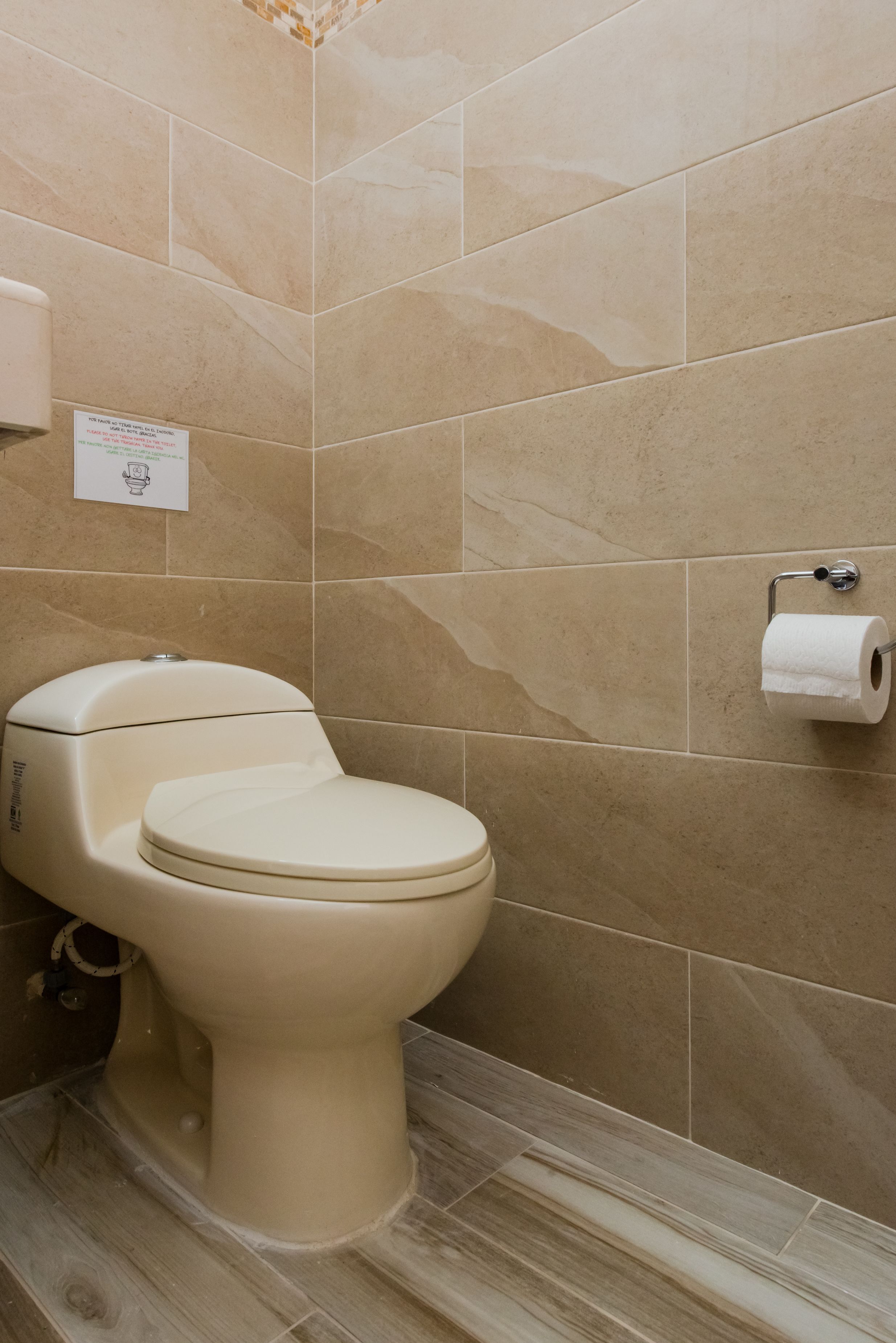 Une salle de bain avec des toilettes, des carreaux de couleur beige et un porte-rouleau de papier toilette.