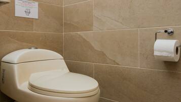 Une salle de bain avec des toilettes, des carreaux de couleur beige et un porte-rouleau de papier toilette.