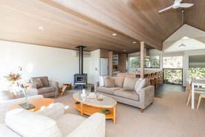 A spacious living area with a fireplace, sofas, and a dining area with natural light. - Top Deck (Lorne)