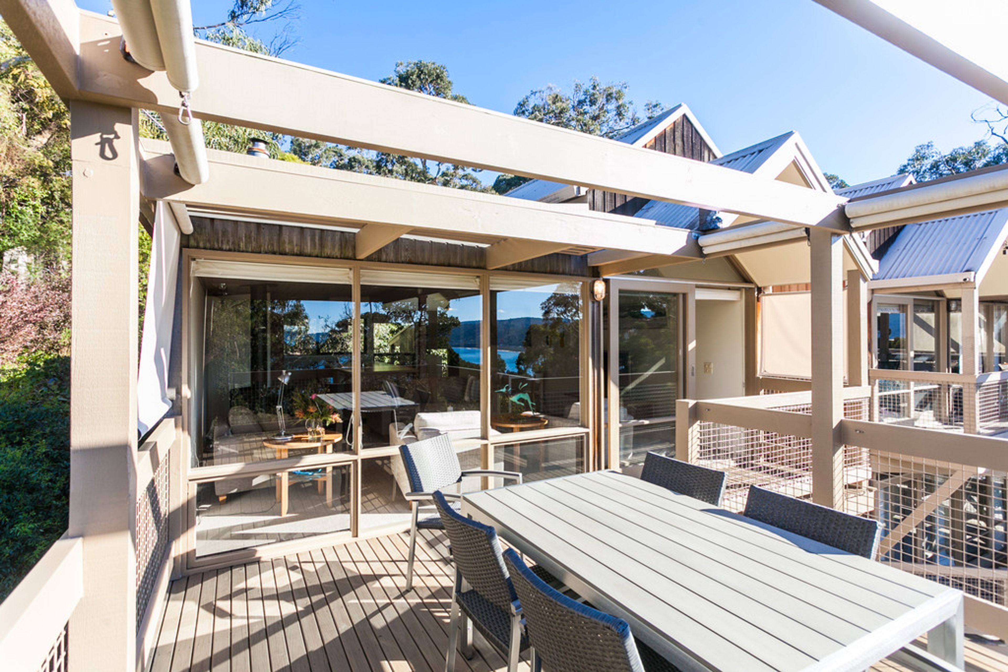 A covered outdoor area with a table and chairs, glass doors leading to an interior space, and a view of the surrounding landscape.