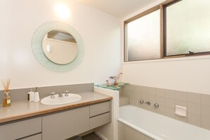 A bathroom with a round mirror, a sink, a bathtub, and a window. - Top Deck (Lorne)