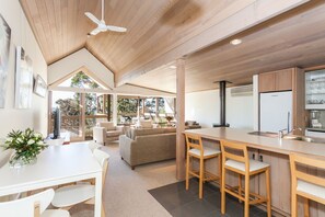 A modern kitchen with a central island, a dining area with a white table and chairs, and a cozy seating area with a sofa and chairs.