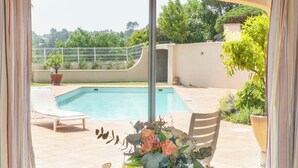 Et spisebord dækket med morgenmad, en blomstervase og udsigt til pool og have.