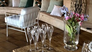 Ein gemütlicher Sitzbereich mit einer Couch und Sesseln, einem Holztisch mit Weingläsern und einer Vase mit Blumen.