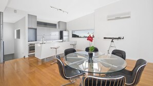 A modern kitchen with white cabinets, a central island, and a dining area with a glass table and metal chairs. - The Lookout 3BR with Ocean views (Apollo Bay)