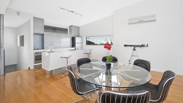 A modern kitchen with white cabinets, a central island, and a dining area with a glass table and metal chairs.