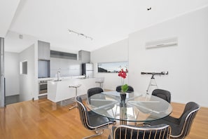 A modern kitchen with white cabinets, a central island, and a dining area with a glass table and metal chairs. - The Lookout 3BR with Ocean views (Apollo Bay)