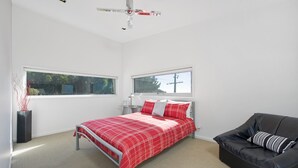 A bedroom with a bed, a black leather sofa, and two windows. - The Lookout 3BR with Ocean views (Apollo Bay)