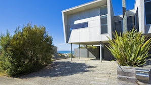A modern two-story building with a flat roof, large windows, and a gravel driveway.
